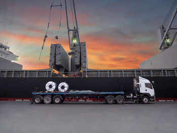 Semi-truck by ship moored at harbor during sunset