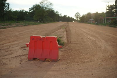 Red road amidst trees on field against sky