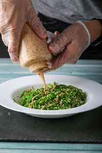 Close-up of person pouring green salad in plate on table