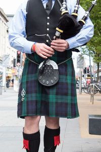 Midsection of man holding bagpipe in city