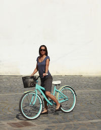 Full length of woman with bicycle against wall on street