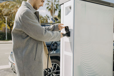 Young man plugging car charger at charging station