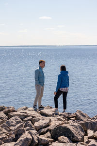 Two friends, a man and a woman, are standing on rocks near the water of a lake or sea 