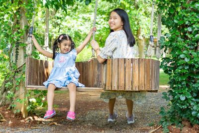 Portrait of mother and daughter sitting on swing at park