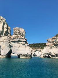 Rock formations by sea against clear blue sky