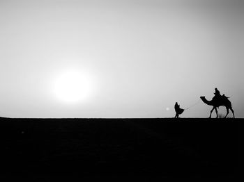 Silhouette people riding horse on desert against sky