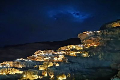 Illuminated buildings by sea against sky at night