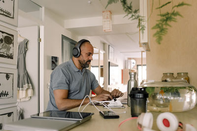 Businessman wearing headphones working on laptop while sitting at kitchen island