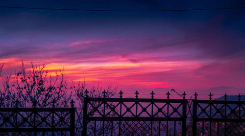 Silhouette railing by sea against sky during sunset