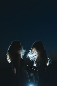Silhouette women standing against illuminated background against sky during dusk