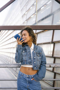 Young woman in denim jacket sending voicemail though smart phone