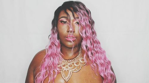 Portrait of young woman with dyed hair wearing necklace against white background