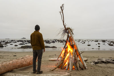 Rear view of hiker looking at view while standing by bonfire at olympic coast against clear sky