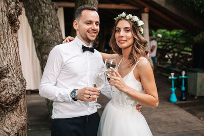 Portrait of couple with arm around holding wineglasses while standing outdoors