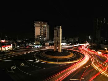 Light trails on road amidst buildings against sky at night