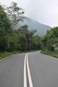 Empty road by trees against sky