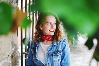 Smiling young woman standing on footpath by brick wall 