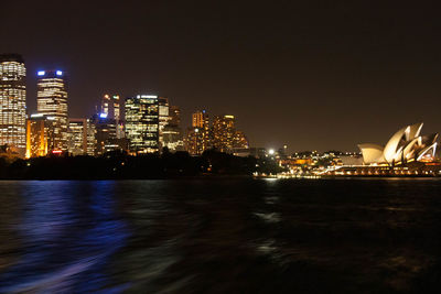 Illuminated buildings by sea against sky at night