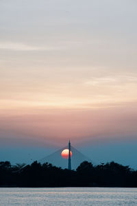 Silhouette tower by lake against sky during sunset