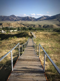 Footbridge leading to mountains against sky