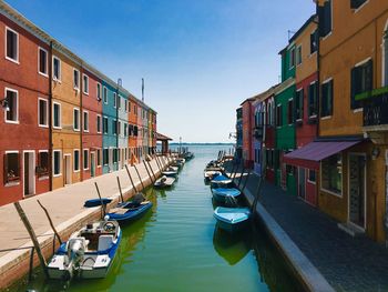 Boats moored in canal amidst buildings against sky