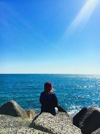 Rear view of woman sitting on rock against sea