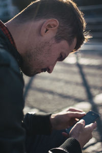 Serious young man using smart phone while sitting by street