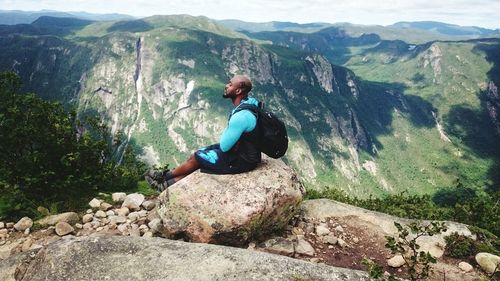 Side view of man sitting on rock against mountain range