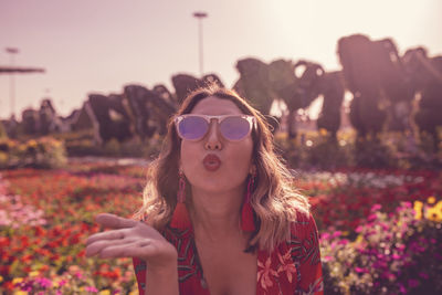 Young woman blowing kiss while standing in ornamental garden 