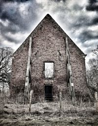 Abandoned house on field against cloudy sky