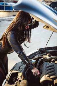 Side view of fashionable woman repairing car engine
