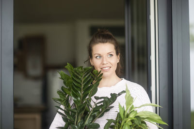 Young woman carrying potplant outside at home