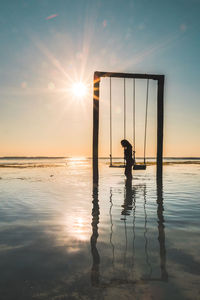 Silhouette woman with swing in sea against sky during sunset