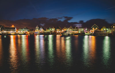 Illuminated buildings at harbor against sky at night