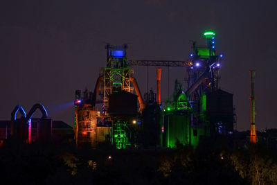 Low angle view of illuminated industry against clear sky at night