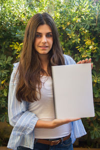 Portrait of woman holding spiral notebook against plants