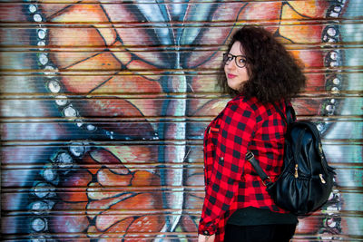 Portrait of woman standing by graffiti wall