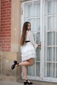 Side view of young woman standing against brick wall