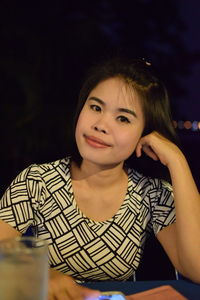 Portrait of young woman sitting against sky at outdoor cafe during night