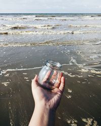 Cropped hand of person holding jar on beach