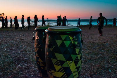 Drums at beach with people in background during sunset