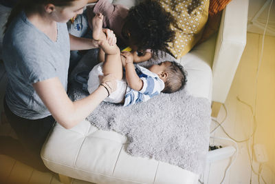 Boy playing while mother dressing son at sofa