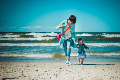 Mother and daughter walking at beach against blue sky