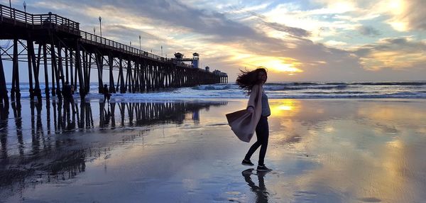 Woman standing at beach against sky during sunset