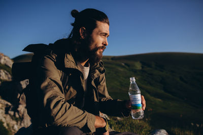 Young man drinking water while sitting on bottle against sky
