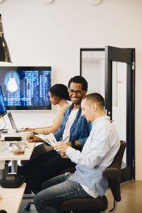 Male programmers discussing while female working in background at creative office