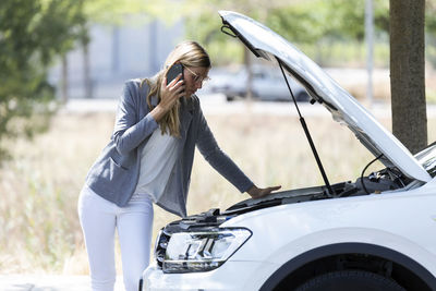 Stressed young woman calling for assistance after breaking down car