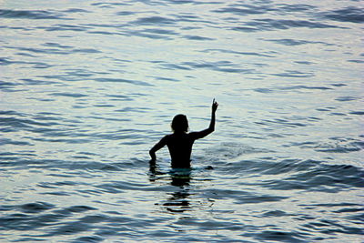 Rear view of silhouette man with arm raised at sea