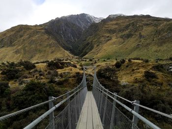 Footbridge over mountain against sky