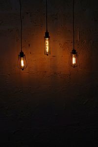 Illuminated light bulbs hanging against wall in darkroom